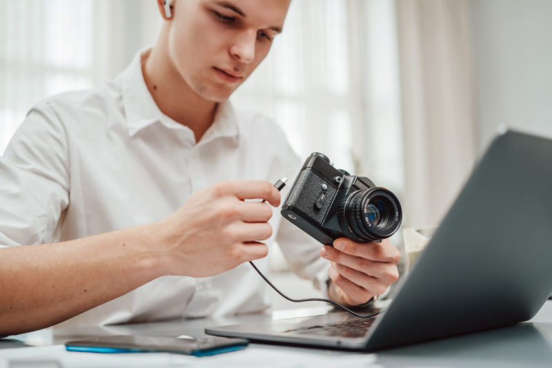 Jonge fotograaf sluit zijn fotocamera aan op laptop in kantoor